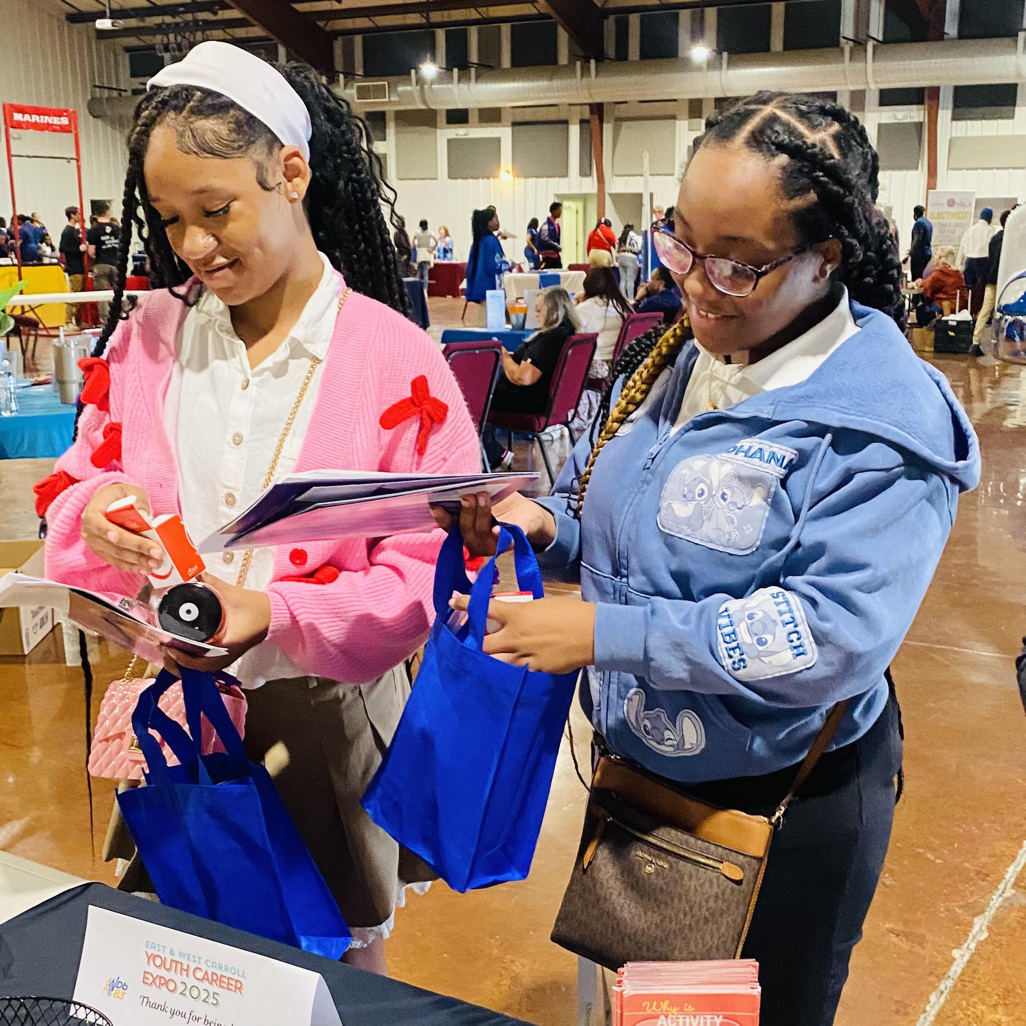 Two teen girls looking at items they picked up off a table.